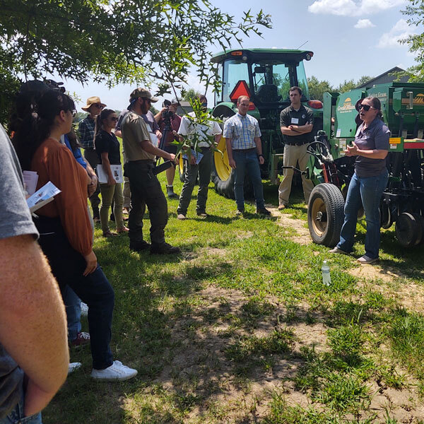 Person talking to a group of people in a field next to tractors